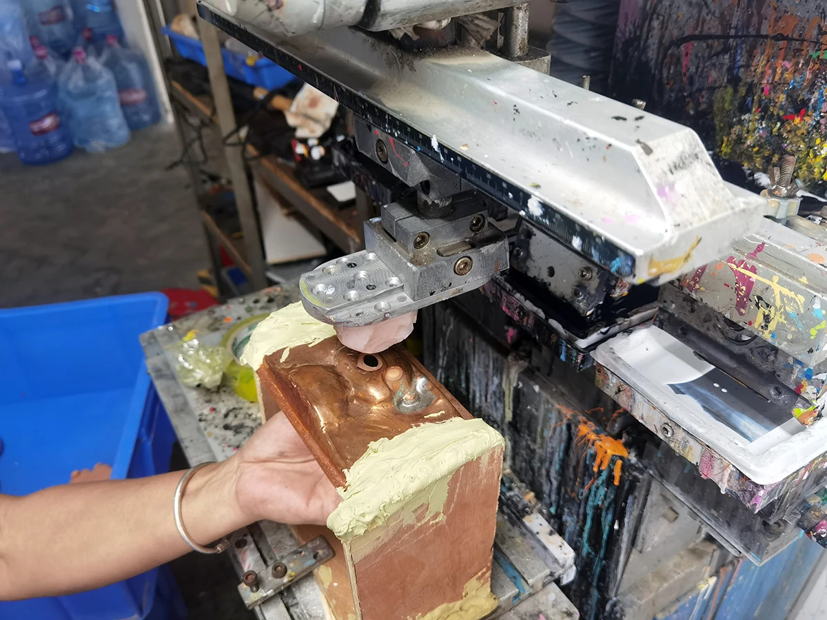 A vinyl figure shaped like a teddy bear is having its eyes printed using the pad printing process.